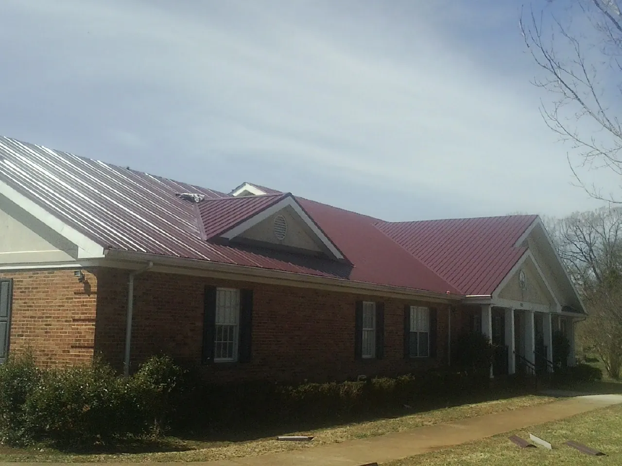 Red metal roof with gabled entries on a long brick building, from a Hail Damage Roof Repair job in Idleyld Park