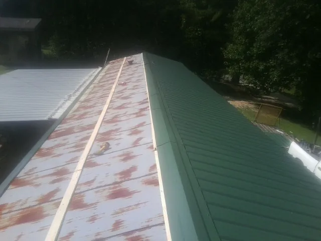 Old rusted panels beside newly installed green metal roofing — Wind Damage Roof Repair by Roofing Brothers in Idleyld Park