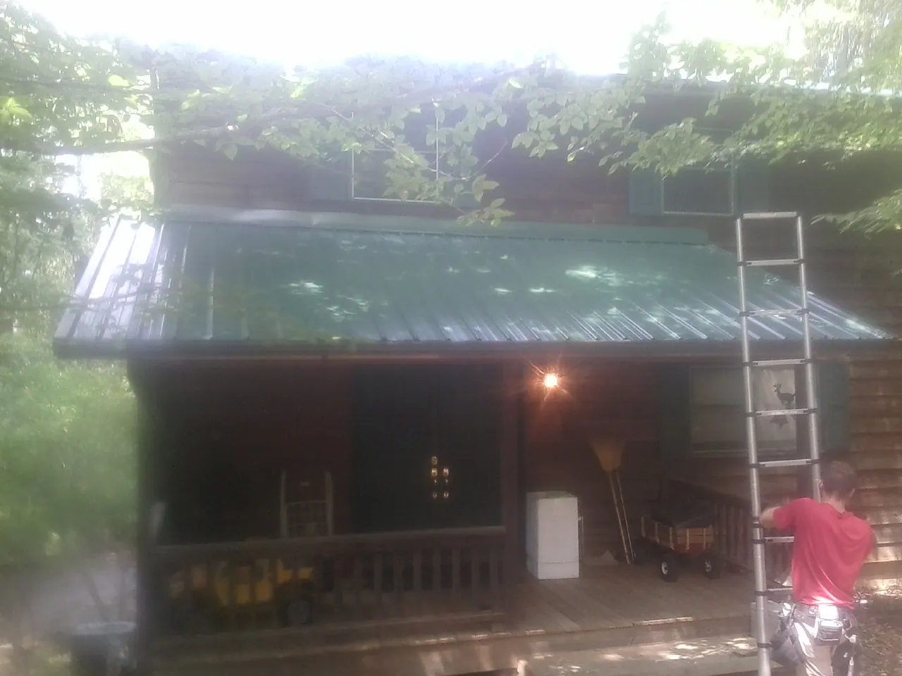 Worker on a ladder at the green porch roof of a wooded cabin in Idleyld Park