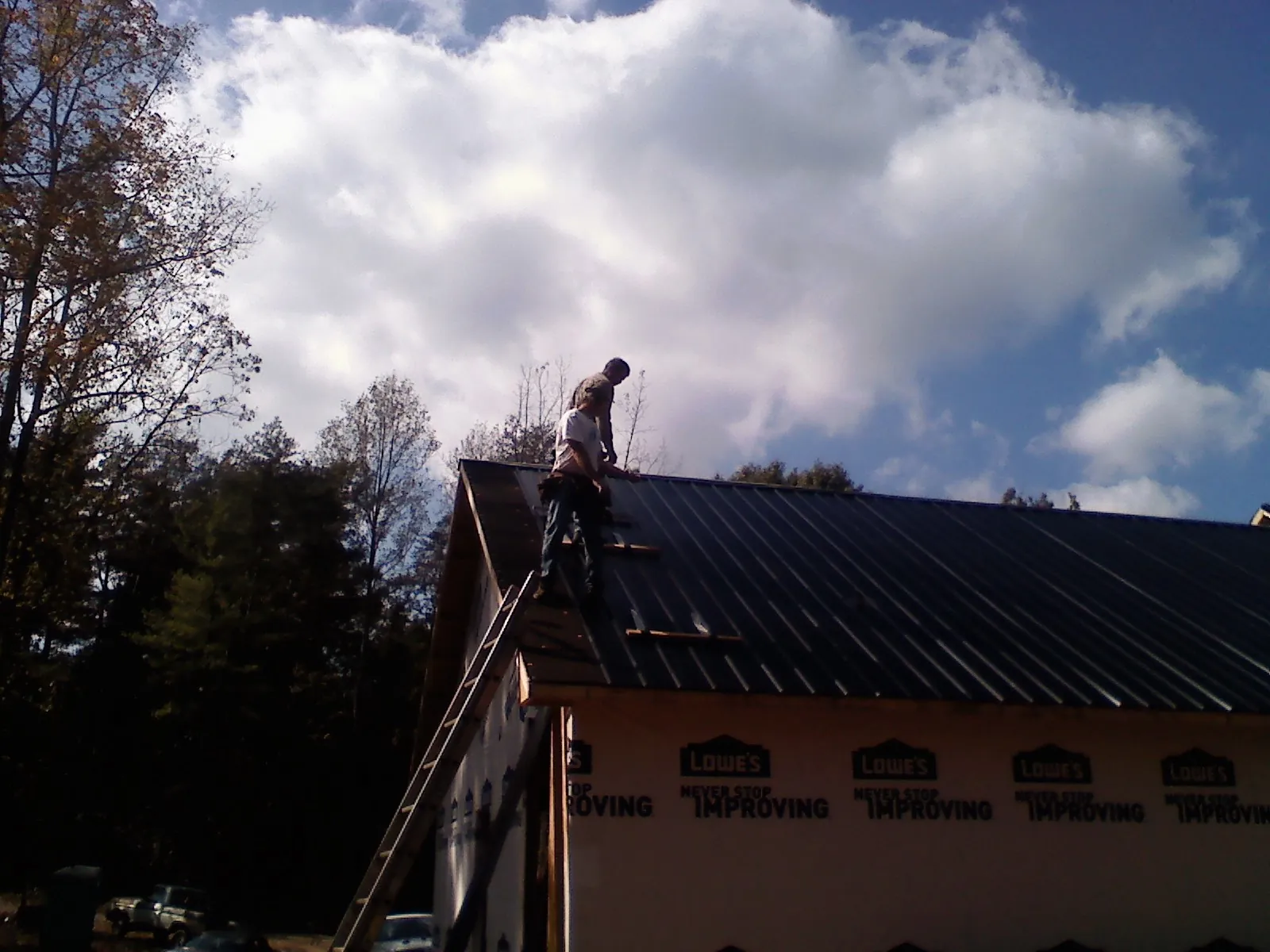 Roofer fastening dark metal panels high against a cloudy sky, from a Roof Inspection job in Idleyld Park