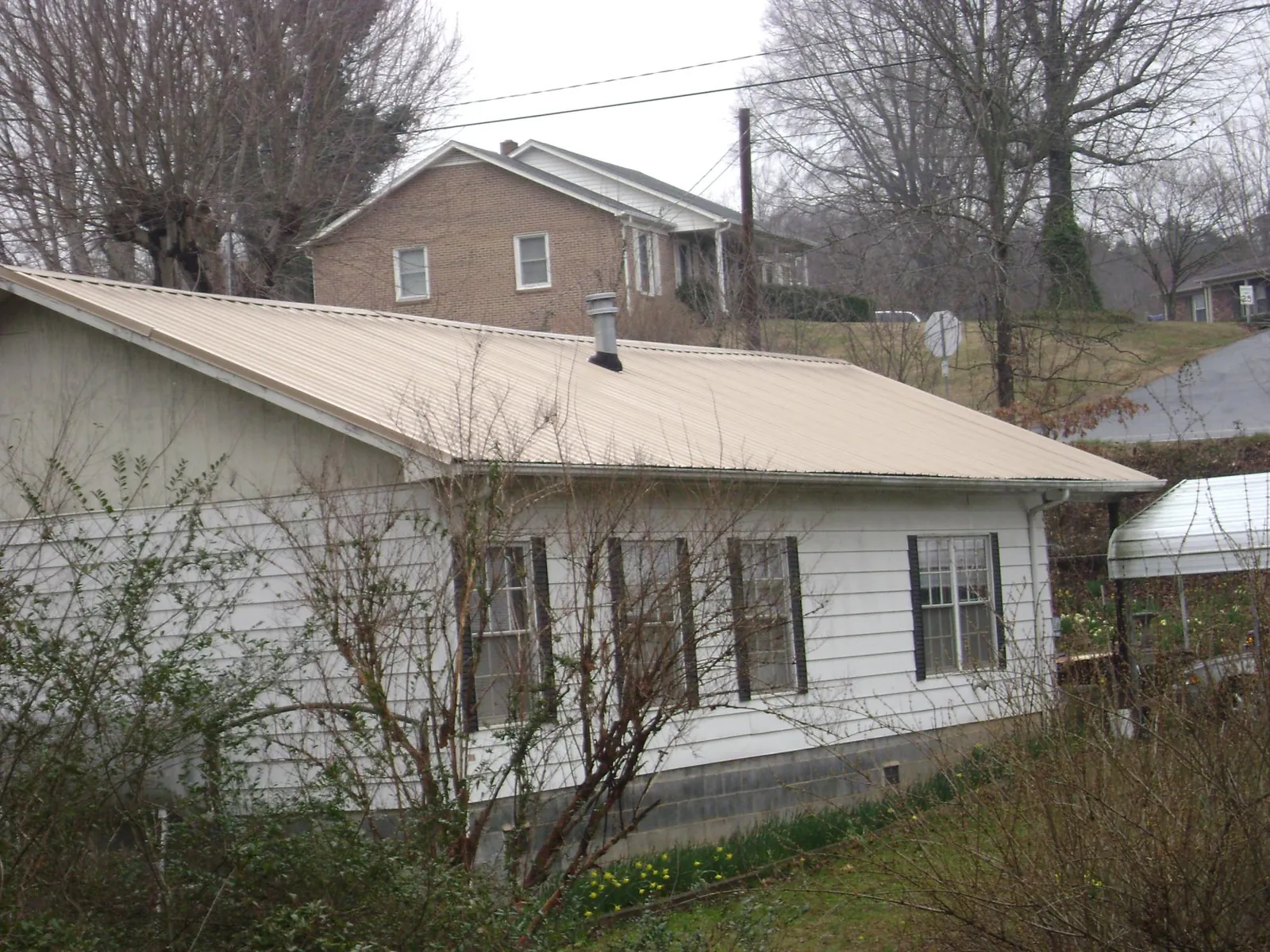 Tan metal roof on a white sided house set into a hillside — Commercial Roofing by Roofing Brothers in Idleyld Park